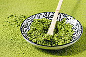 Green tea matcha powder in ceramic bowl with traditional bamboo spoon over powdering matcha as background
