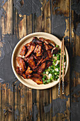 Chinese traditional dish Cantonese BBQ Pork Belly with spring onion served in ceramic plate with chopsticks over dark wooden plank background