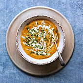 A bowl of thick homemade pumpkin soup with a spoon on a wooden serving plate