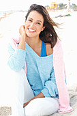 Brünette Frau in blauem Oversize-Pulli, darüber rosa Pulli und weißer Hose