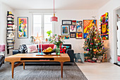 Coffee table in front of black leather sofa in living room with Christmas tree in corner and comic-style artworks on wall