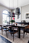 Dunkler Esstisch mit Stühlen, darüber Hängelampen aus alten Fischerkörben im Zimmer mit weiß gestrichener Ziegelwand