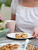A woman sitting at an outdoor brunch with a coffee cup, plate of cinnamon buns and flowers