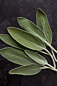 Individual sage leaves on a textured black countertop, photographed from above