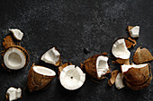 Aufgebrochene Kokosnüsse auf dunklem Untergrund (Aufsicht)