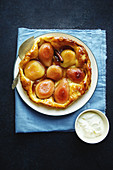 Overhead shot of tart tatin with pears and whipped cream on dark blue background