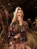 A blonde woman wearing wearing a floral patterned, autumnal blouse