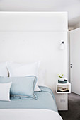 Double bed with white and light blue bed linen in front of the room divider in the bedroom