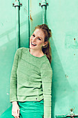 Junge Frau in grünem Pullover und grüner Hose vor grünem Hintergrund