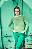 Junge Frau in grünem Pullover und grüner Hose vor grünem Hintergrund