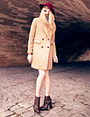 A blonde woman wearing a dark red hat and a sand-coloured coat