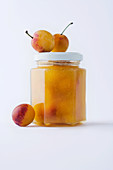 A jar of yellow plum jam against a white background