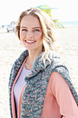 A blonde woman wearing an apricot cardigan with a jumper over her shoulders