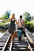 A young couple with a suitcase and a guitar on a railway track