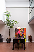 Dark wooden table and chairs, standard lamp, large painting and potted tree in interior with high ceiling