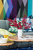 Vase with leaf sprigs on coffee table, sofa in front of colorful wallpaper