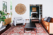 Sideboard, upholstered armchair, leather couch and coffee table in the living room, view through an open passage to the bookcase and dining area