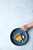 A plate with a piece of quiche with a little child hand on a white surface