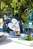Tischdekoration mit Karte in Herzform und blauen Glasvasen mit Blumen