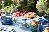 Gedeckter Tisch im Freien mit Obstkuchen, Blumen und Artischocken in Glasvasen