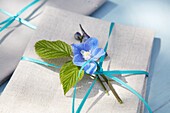 Geschenkverpackung mit blauer Blüte und grünen Blättern auf Leinenstoff