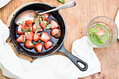 Strawberries grilled in sugar with basil on a wooden table with a glass of water with mint