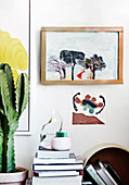 Bücherstapel und Kaktus auf Schreibtisch, darüber Bild