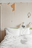 Weiße Bettwäsche auf Doppelbett, darüber Leselampe und Traumfänger an Wand mit abgeblätterter Tapete