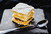 Close up of served dessert made of puff pastry and various creams topped with sugar powder