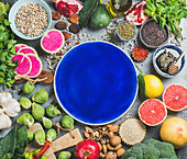 Stillleben mit Gemüse, Obst, Samen, Getreide, Gewürzen, Superfoods und Kräutern um einen blauen Teller