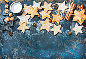 Gingerbread Christmas star shaped cookies with cinnamon, anise, nuts, baking molds and sugar powder on dark plywood painted background