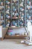 Pyramid shelves and rocking horse in child's bedroom with colourful wallpaper