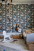 Rocking horse, gymnastic rings and wooden bed in child's bedroom with colourful wallpaper