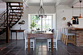 White chairs at wooden table in open-plan interior with staircase