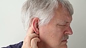 Man rubbing behind his ear in pain