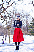 A young woman wearing a blue hat and scarf, a blue jumper and a red skirt in a wintery park