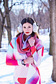 A young woman wearing a geometric patterned dress and earmuffs in a wintery park
