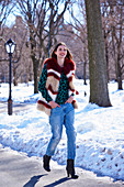 A young woman wearing a shirt, red striped faux fur boots and jeans in a snowy park