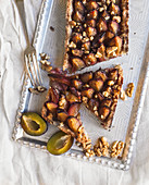Plum pie with walnuts on a silver tray over a white linen fabric surface