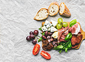 Smoked meat, sausages, cheese, grapes, cherry-tomatoes, olives, basil leaves, arugula, dried tomatoes and baguette slices