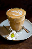 Caffe Latte im Glas mit weisser Blume auf Untertasse
