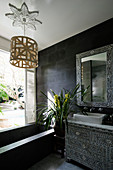 Chest of drawers and mirror frame with mother-of-pearl inlays in black bathroom with bathtub