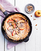 An apple pancake with pecan nuts and icing sugar in a cast iron pan