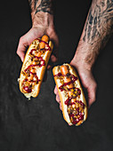 A man holding two hot dogs with onions and ketchup