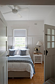 Blick aufs Bett mit blau-weißer Bettwäsche und Nachttisch im Schlafzimmer mit Dielenboden