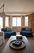 Große Sitzsäcke mit blauem Bezug und Couchtisch im Wohnzimmer mit Erker und Natursteinwand