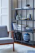 Offenes Metallregal mit Büchern und verschiedenen Keramikgefässen, daneben Stuhl mit grauem Stoffbezug