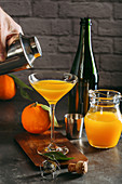 Mimosa (Cocktail mit Champagner und Orangensaft) aus Shaker in Gläser gießen