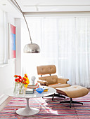 Round white table and classic Eames Lounge Chair with pale leather cover on striped rug