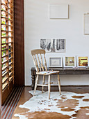 Rustikale Holzbank mit Bildersammlung und Holzstuhl auf Tierfellteppich vor Lamellenfenster